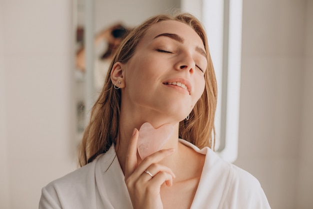 Femme faisant l'auto-massage avec la pierre de gua sha de quartz rose