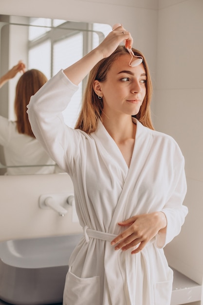 Femme faisant un auto-massage avec un rouleau facial en quartz rose