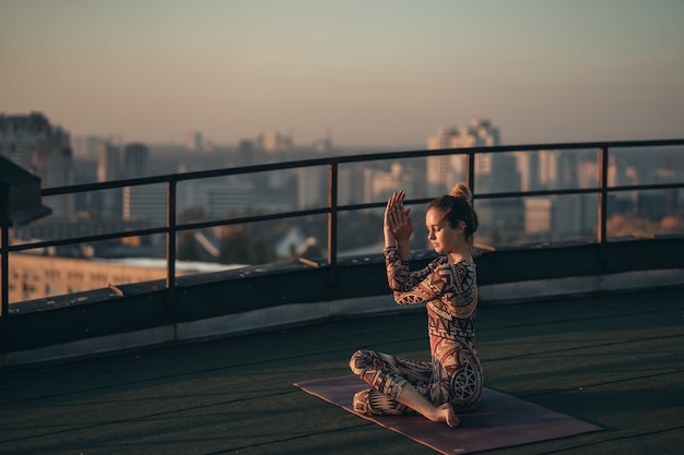 Femme faisant du yoga sur le toit d'un gratte-ciel dans la grande ville.