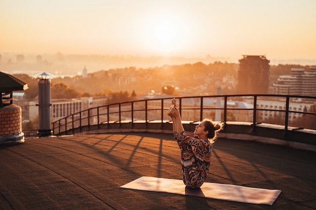 Femme faisant du yoga sur le toit d'un gratte-ciel dans la grande ville.