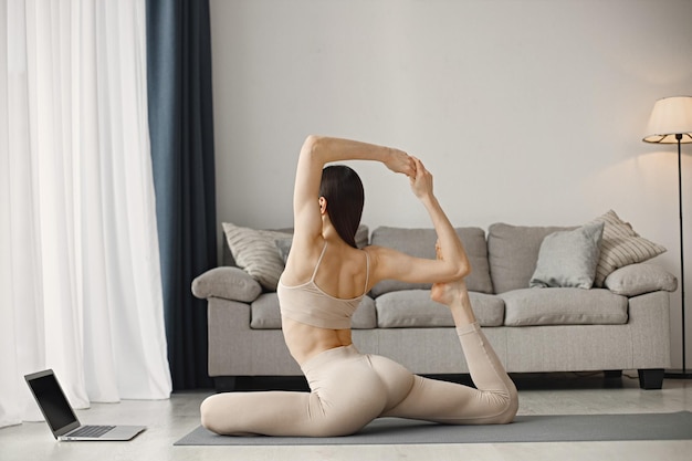 Femme faisant du yoga tout en regardant des tutoriels d'entraînement en ligne sur un ordinateur portable à la maison