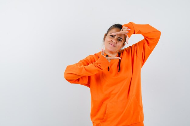 Femme faisant un geste de cadre en sweat à capuche orange et semblant joyeuse