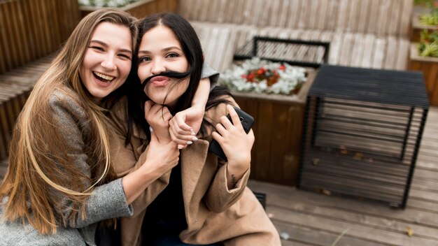 Femme faisant une moustache avec ses cheveux à côté de son amie