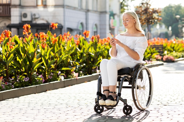 Photo gratuite femme en fauteuil roulant dans la ville à l'aide de smartphone avec espace de copie