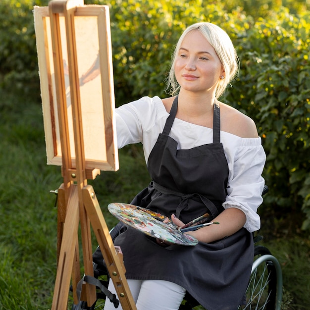 Femme en fauteuil roulant à l'extérieur dans la nature avec toile et palette