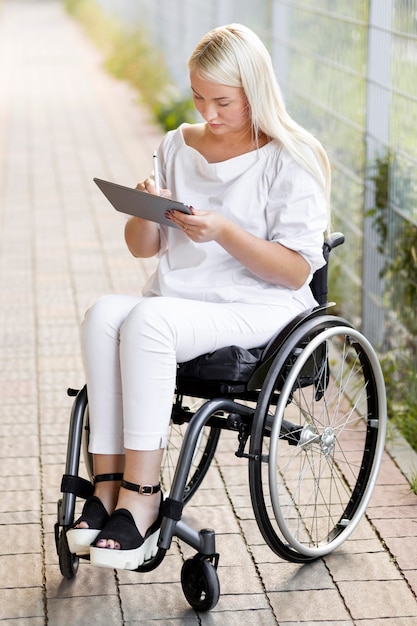 Femme en fauteuil roulant à l'extérieur avec tablette