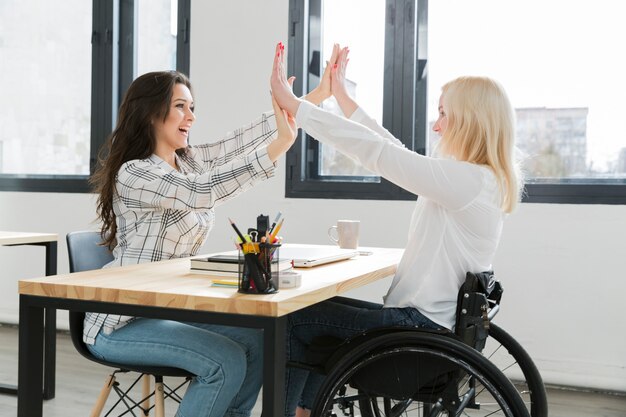 Femme en fauteuil roulant high-fiving avec son collègue