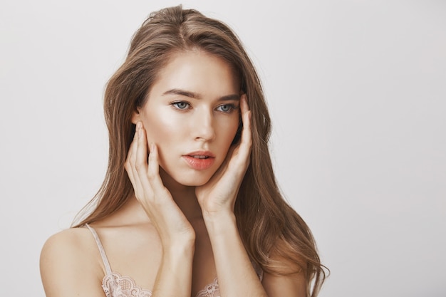 Une femme féminine et tendre a l'air bien et touche une peau propre