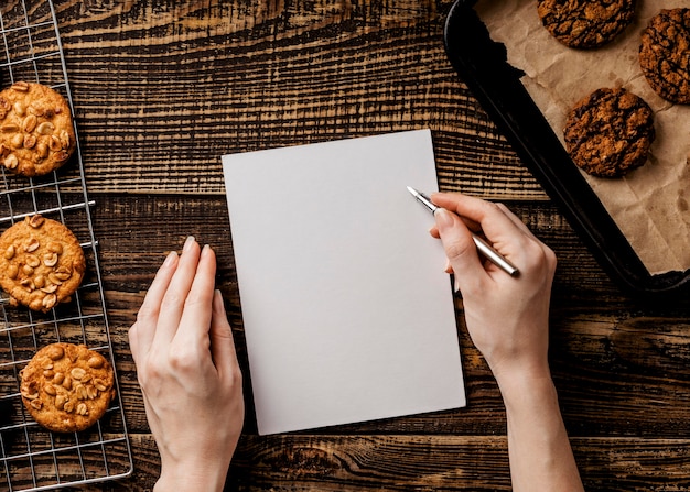 Photo gratuite femme avec feuille de papier et délicieux cookies sur table