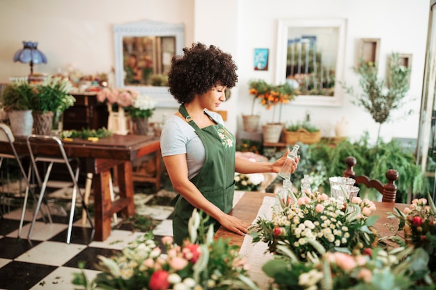 Femme fleuriste tenant une bouteille en verre dans la boutique