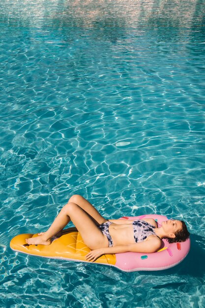 Femme flottant sur un matelas gonflable dans la piscine