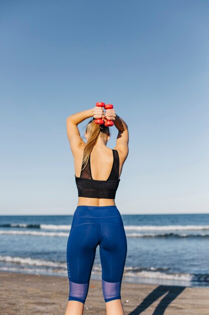 Femme de formation avec des haltères à la plage