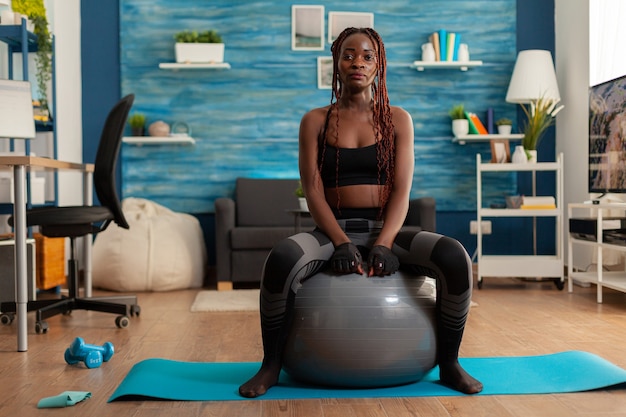 Femme forte active sportive assise sur un ballon de stabilité au repos, après un entraînement intense dans le salon de la maison