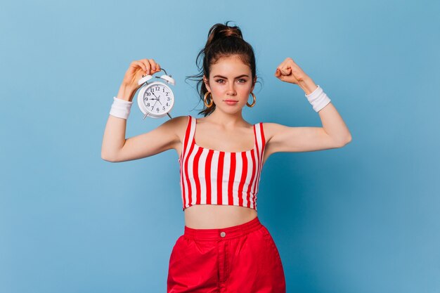 Femme forte en tenue rayée rouge et blanche montre la force de ses mains