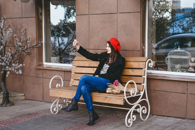 Photo gratuite femme française dans un béret rouge sur un banc de rue