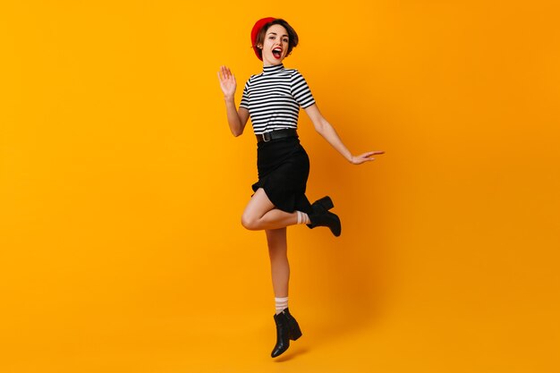 Femme française insouciante en jupe danse sur mur jaune