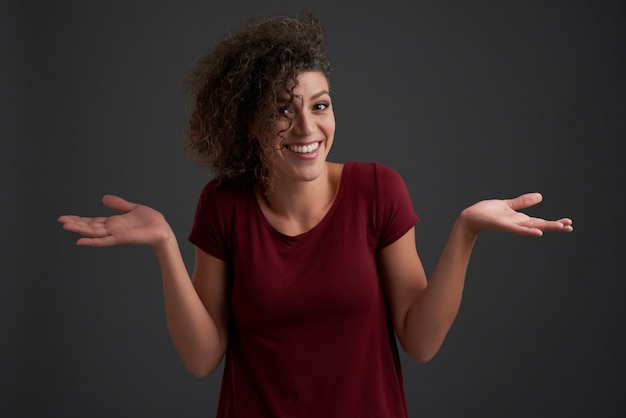 Femme frisée haussant les épaules à la caméra contre gris foncé