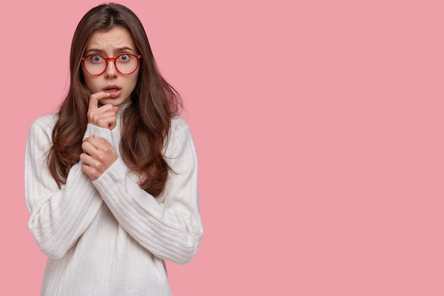 Une femme frustrée a une expression faciale nerveuse garde la main près de la bouche, regarde avec perplexité