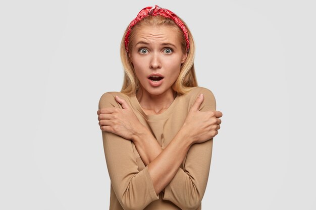 Une femme frustrée halète de peur, frissonne à l'intérieur, garde les mains croisées sur la poitrine, remarque quelque chose de terrible