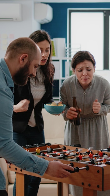 Photo gratuite femme gagnant un match de football au baby-foot tout en jouant avec un homme au bureau, s'amusant après le travail. collègues multiethniques jouant pour se divertir, dégustant des boissons à la bière.