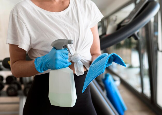 Femme avec des gants tenant une solution de nettoyage au gymnase