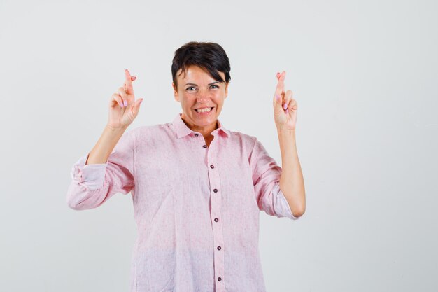 Femme gardant les doigts croisés en chemise rose et à la recherche de bonne humeur. vue de face.