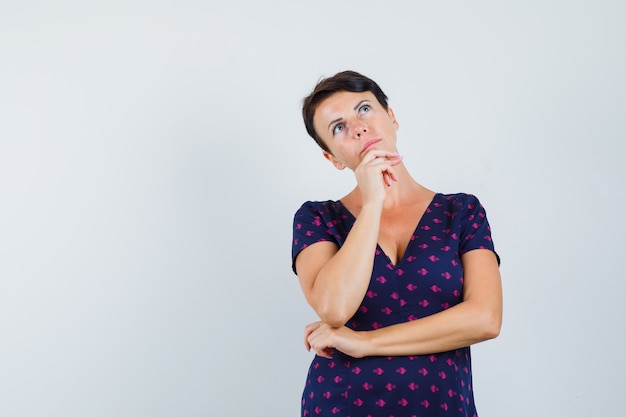 Femme gardant la main sur le menton en robe et à la recherche indécise.