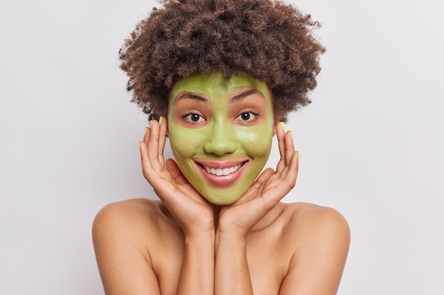 la femme garde la main sur le visage applique un masque de concombre vert pour des poses nourrissantes pour la peau topless on white