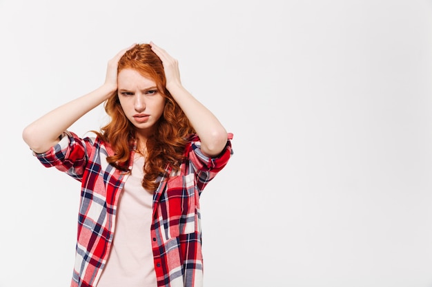 Femme gingembre confus en chemise tenant la tête et en détournant les yeux