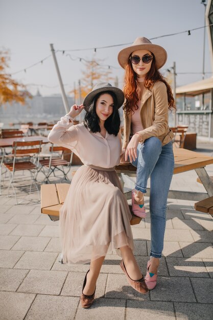 Femme gracieuse en jupe longue assis dans un café de rue avec meilleur ami