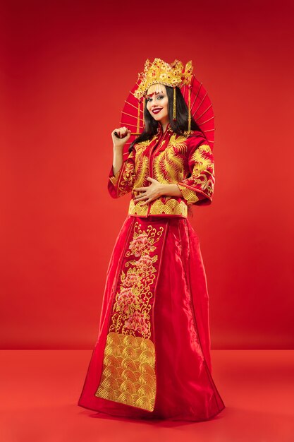 Femme gracieuse traditionnelle chinoise au studio sur fond rouge. Belle fille portant le costume national. Nouvel an chinois, élégance, grâce, interprète, performance, danse, actrice, concept vestimentaire