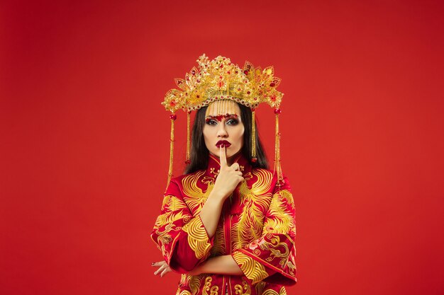 Femme gracieuse traditionnelle chinoise au studio sur fond rouge. Belle fille portant le costume national. Nouvel an chinois, élégance, grâce, interprète, performance, danse, actrice, concept vestimentaire