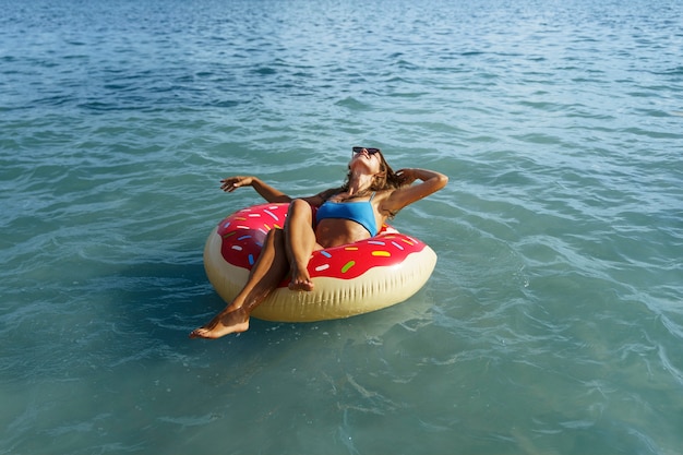 Femme grand angle allongée sur un flotteur de beignet