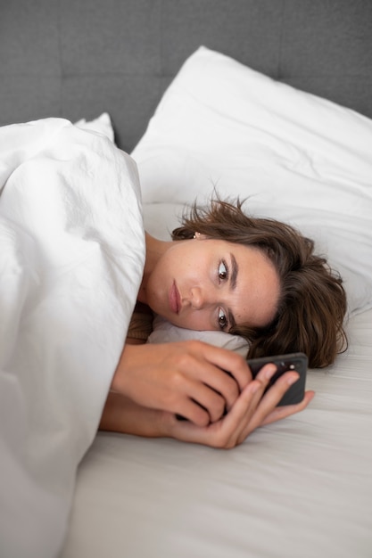 Photo gratuite femme grand angle au lit avec smartphone