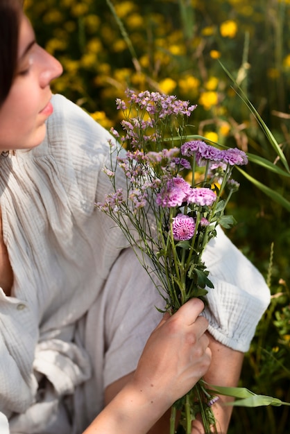 Photo gratuite femme grand angle tenant des fleurs violettes