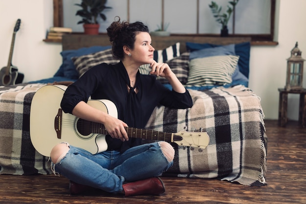 Femme à la guitare assis devant le lit