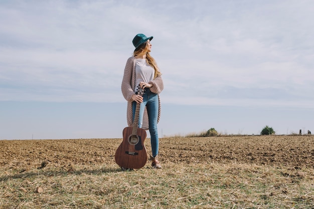 Femme avec guitare debout dans le champ