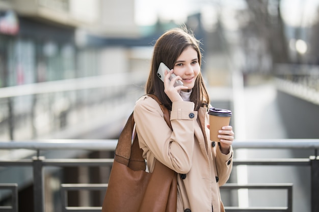 Femme habillée décontractée marchant dans la rue tenant une tasse de café et un téléphone