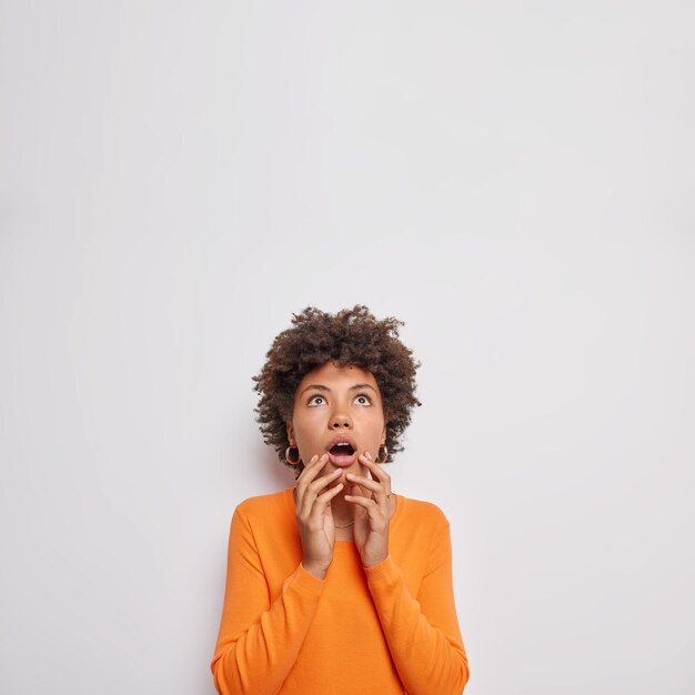 une femme halète d'étonnement garde la bouche grande ouverte remarque quelque chose d'horribe vêtu d'un pull orange décontracté isolé sur un espace de copie blanc