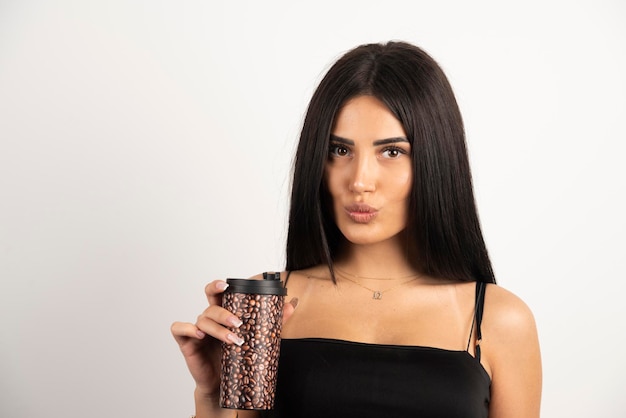 Femme en haut noir tenant une tasse de café sur fond beige. Photo de haute qualité