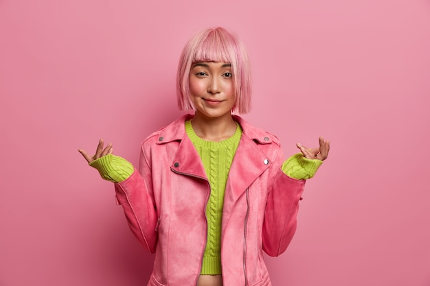 Photo gratuite une femme hésitante inconsciente avec une coiffure bob rose lève la main perplexe, n'a aucune idée de ce qui se passe