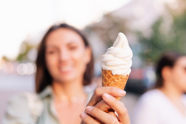 Femme à l'heure du coucher du soleil d'été ayant un cornet de crème glacée dans la rue de la ville