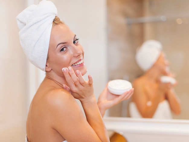 Femme heureuse, appliquer une crème hydratante sur le visage après la douche