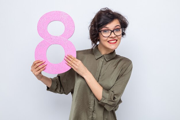 Femme heureuse aux cheveux courts tenant le numéro huit en carton à la recherche de sourire joyeux célébrant la journée internationale de la femme le 8 mars