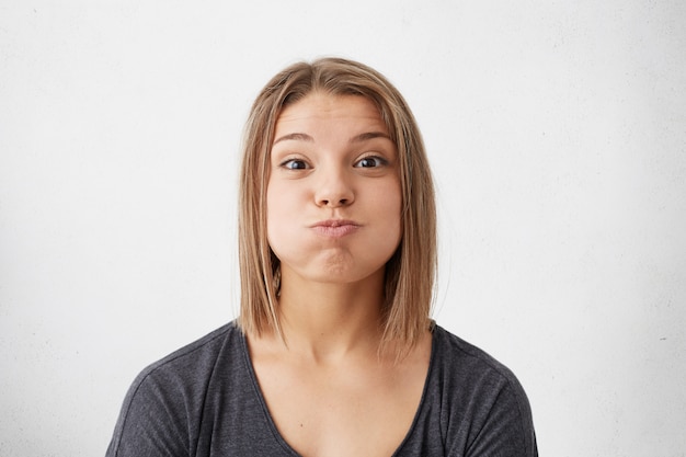 Photo gratuite femme heureuse aux yeux noirs peau pure et coiffure bob soufflant ses joues avec plaisir en s'amusant. belle femme ayant la bonne humeur faisant la grimace montrant ses émotions.