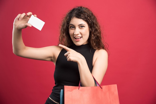 Femme heureuse avec beaucoup de sacs et carte bancaire sur rouge