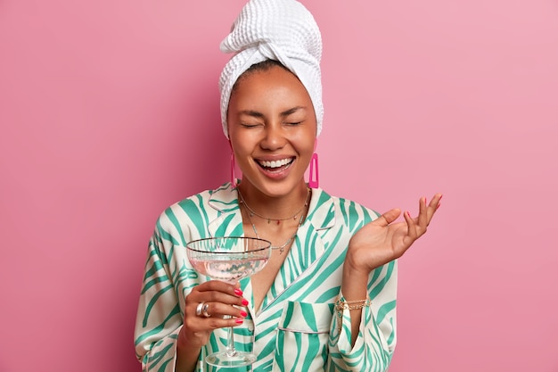 femme heureuse avec une beauté naturelle, une peau foncée, un teint bien soigné, jouit d'une atmosphère domestique, boit un cocktail après avoir pris un bain, vêtue de vêtements confortables, se détend à la maison