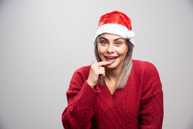 Femme heureuse en bonnet de Noel posant sur fond gris.