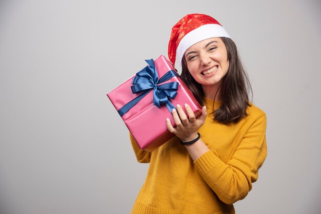 Femme heureuse en bonnet de Noel tenant une boîte-cadeau.