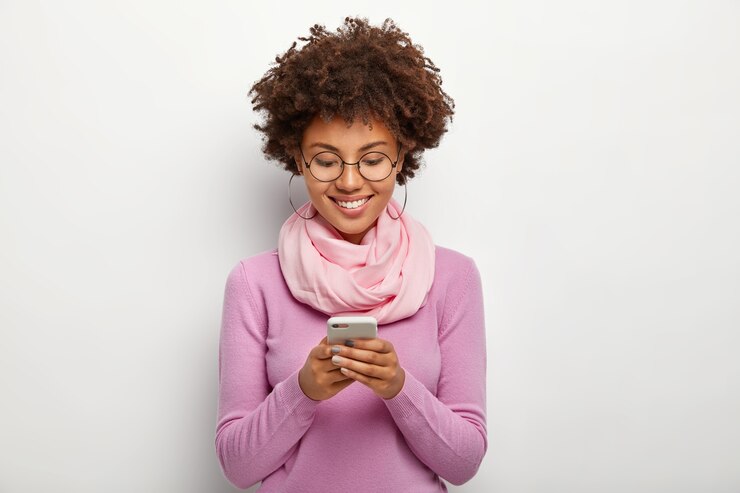 Photo gratuit femme heureuse concentrée sur un smartphone, a une expression joyeuse, vérifie la notification ou la boîte e-mail, porte des lunettes et des vêtements lumineux